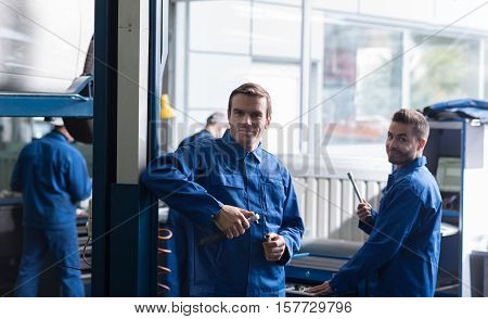 Will make it perfect. Positive professional adult mechanics holding tools and standing in garage while going to repair a car
