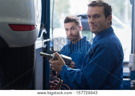 every day work. Professional mechanic changing car wheel and using pneumatic wrench while reparing car with his colleague
