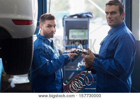 Reliable service. Professional delighted car mechanic holding pneumatic wrench and changing car wheel while his colleague using tablet in the background
