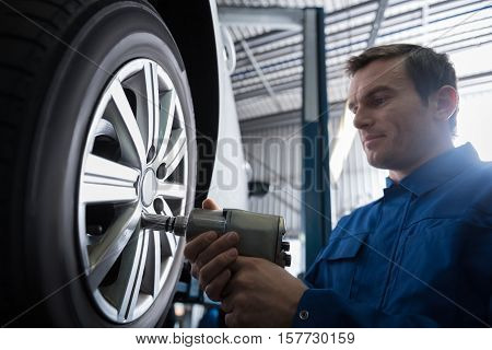 Magic hands. Professional serious mechanic using pneumatic wrench and changing wheel while workign with hisc olleague in auto service