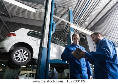 Modern technologies in use. Low angle of positive delighted mechanics using tablet and going to repair car while working in auto service