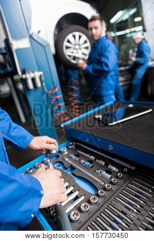 Choose a correct one. Professional car mechanic choosing the right tool while reparing car with his colleague