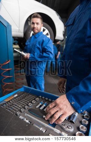 Involved inwork. Professional car mechanic choosing a tool while his colleague standing in the background and going to repair a car