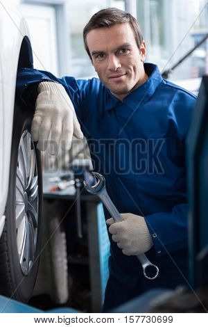 Best service. Professional mechanic holding wrench and chending car tyre while working in car service