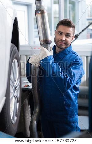 Better change. Positive delighted car mechanic holding muffler and repairing car while working auto service