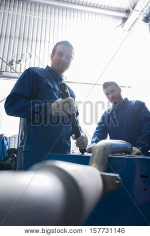 Important work. Low angle of professional car mechanic holding tool while reparing muffler with his colleague