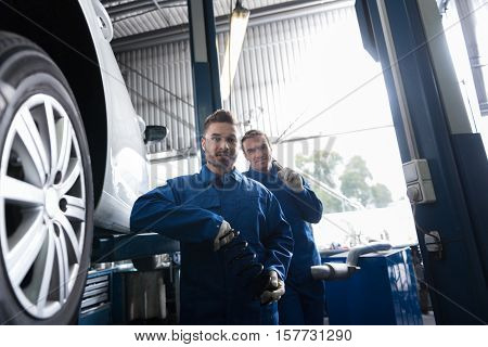 Professional handsome mechanic holding spring and reparing car whle working with his colleague in auto service