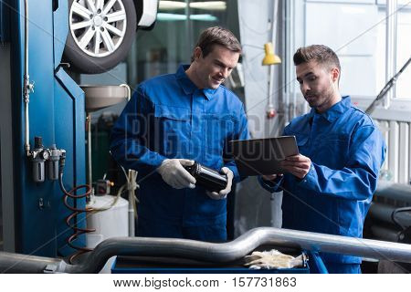 Look here.Positive pleasant mechanics using tablet and talking while reparing car in auto service