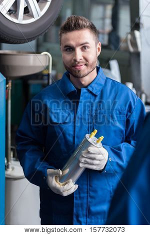 Involved in work. Cheerful handsome auto mechanic holding oil flter and reparing car while workign in auto service