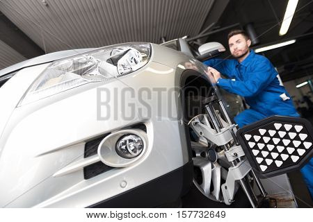 Upgrade it. Professional concentrated mechanic standing near car and adjusting automobile wheel alignment while working in auto service