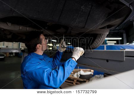 Make it doing well. Pleasant professional mechanic holdign wrench and repating wheel system under the car