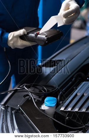 Car meintenance. Professiomal mechanic using special device while checking abilities of auto engine