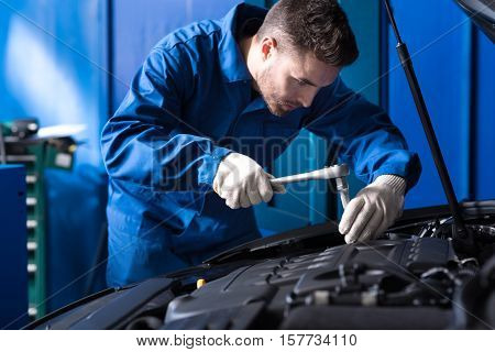 Do it correctly. Professional mechanic using wrenches and repairing car engine while workign in auto service