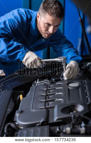 Here is the break out. Concentrated professional mechanic repairing engne and using wrenches while working with car