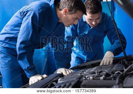 Something is going wrong. Professional serious mechanics examining car engine and repairing break out while working in auto service