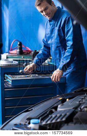 Put everything in order. Pleasant mechanic putting hs tools and resting after repairing car engine