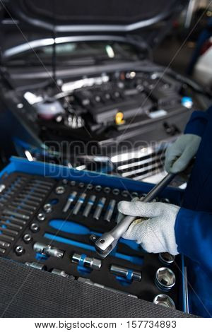 Workign atmosphere. Close up of wrench in hands of professioanl mechanic holdigng it and putting tools in order while working in auto service center
