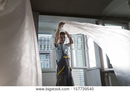 Construction worker wearing worker overall installing protective foil. House apartment renovation. Construction finishing works.