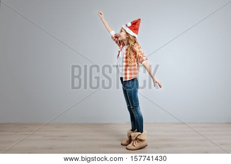 To the rescue. Ceerful little cute girl holding hand up and smiling while standing half turned isolated on grey background