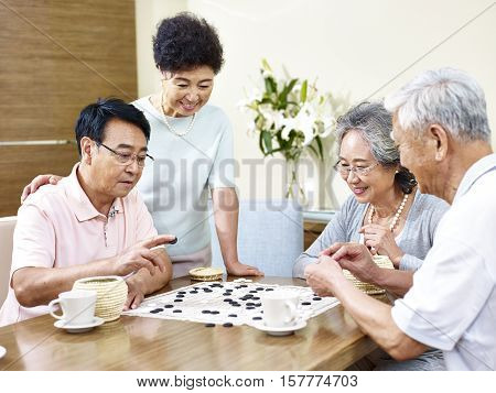two senior men playing Weiqi (or game of go) at home with their wives watching