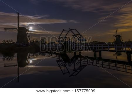 Kinderdijk in the Netherlands with windmills and draw bridge at night with full moon.
