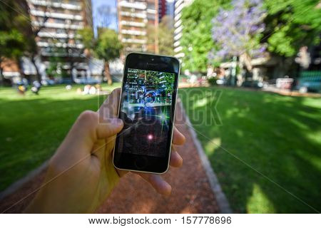 Buenos Aires, Argentina - Nov 11, 2016: Apple iPhone 5c held in one hand showing its screen with Pokemon Go application. Park on the background.