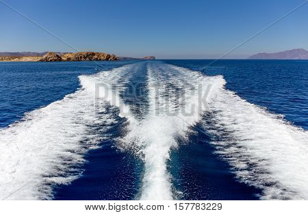 Fast moving boat wake in mediterranean sea and island on background