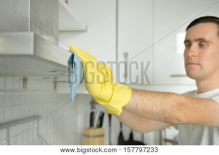 Closeup of male hands in rubber protective yellow gloves cleaning the kitchen metal extractor hood with rag. Home, housekeeping concept