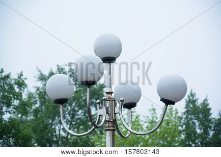 Top side of the lamp post with round plafonds. Green trees on background.