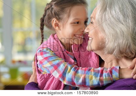 Portrait of smiling grandmother and granddaughter hug and look at each other