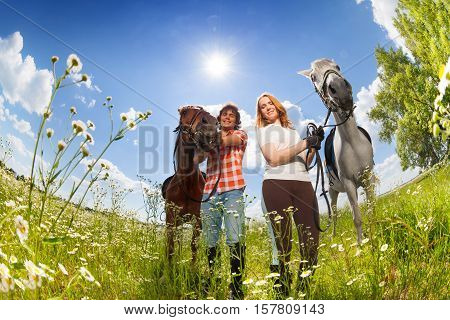 Portrait of young happy couple with their purebred horses walking in flowery meadows at sunny day