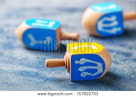 Wooden dreidel for Hanukkah on light sparkling background, close up