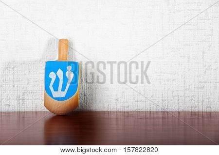 Dreidel for Hanukkah on wooden table against light textured wall