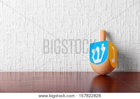 Dreidel for Hanukkah on wooden table against light textured wall