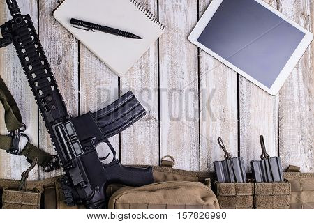 Riflenotebook with penPC tablet touch computerbattle balt with ammo on wooden table.Top view