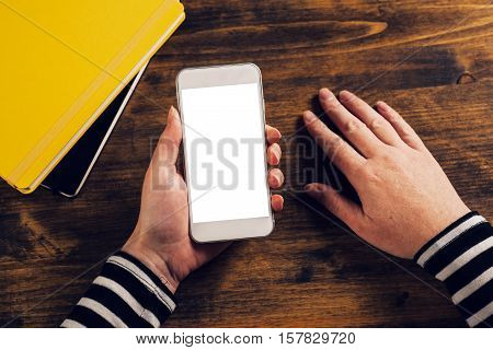 Top view of female hands holding mobile smarthone with blank screen as copy space above office desktop