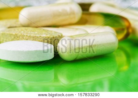 Mixed natural food supplement pills omega 3 calcium multivitamin and glucosamine capsules on green background