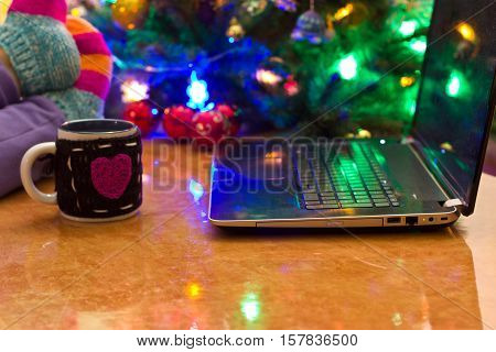 Notebook on the background of the Christmas tree. A cup of tea. Feet in socks on the table.
