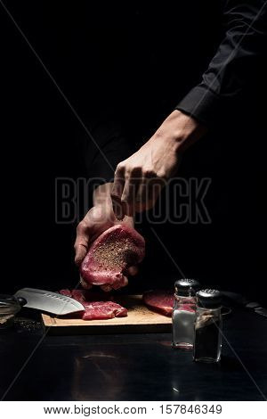 Flavored and tasty. Close up of young male chefs hands spicing the meat while working in restaurant and cooking.