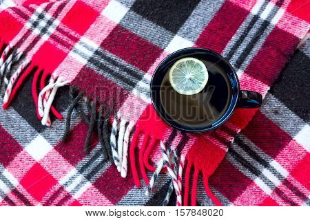 Black cup with tea and lemon standing on warm red checkered plaid. Winter. Cozy home concept.