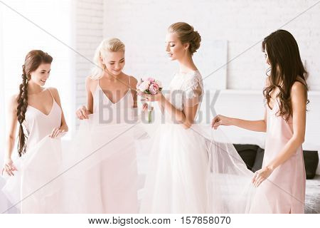 Look at you. Excited smiling young bridesmaids standing in the white bedroom while helping the bride to get ready and expressing excitement