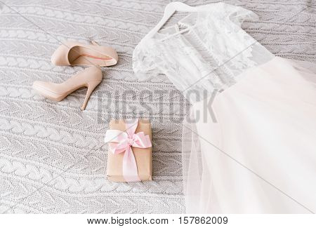 Wedding accessories. White amazing delicate wedding dress and shoes lying on the bed in the bedroom