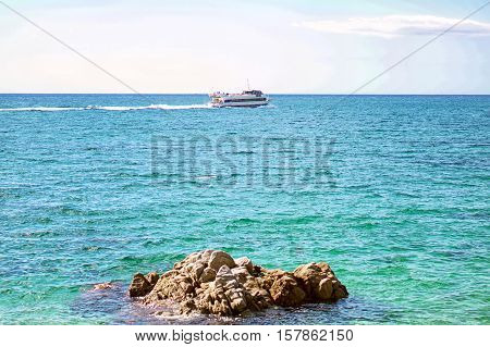 View of a tourist ship liner on deep green blue sea and rock in front.