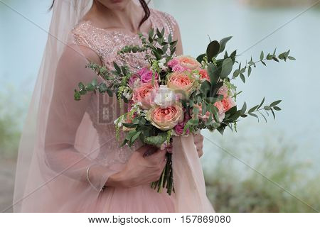 Bride holding a beautiful bridal bouquet. Wedding bouquet of peach roses  single-head pink rose aqua eucalyptus ruscus gypsophila