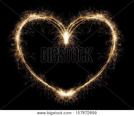 New year party burning sparkler heart shape on black background. Glowing holiday sparkling hand fireworks, love symbol shining fire flame. Christmas light.