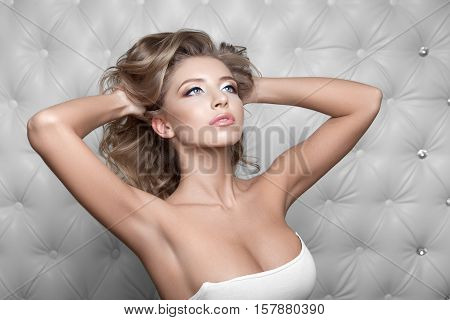 Studio portrait of a sexy blond, over leather upholstery background. Elegant luxury woman with a seductive neckline and bare shoulders looks into the camera.