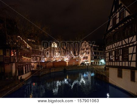 STRASBOURG FRANCE - DEC 6 2016: Christmas market in Place Benjamin Zix with its reflection in the Ill river at dusk with Christmas stalls and people shopping drinking mulled wine