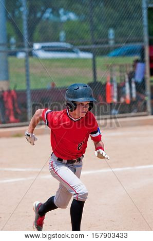 Youth teenage baseball player running to first base.