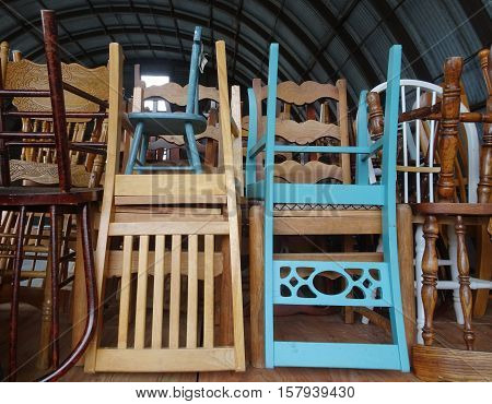 Two antique wooden blue chairs, one adult and one child size, stand out in an array of neatly stacked seats waiting for the next celebration in a rustic setting.