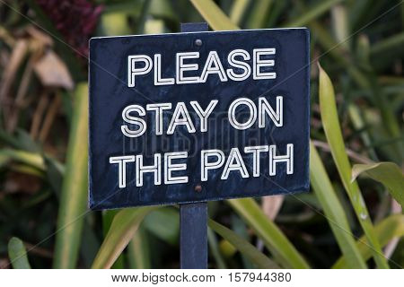 Please stay on path sign in garden with green foliage backdrop.